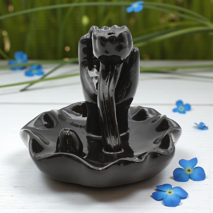 Black ceramic incense burner with water fountain design on a white surface with blue flowers.