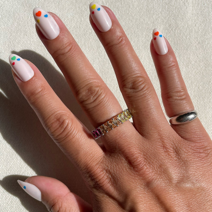 Hand with Rainbow Love | Almond | Medium press-on nails in soft neutral with colorful dot accents on natural skin tone outdoors