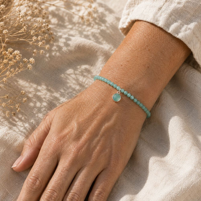 Hand wearing a turquoise beaded bracelet with a small round charm on a neutral background