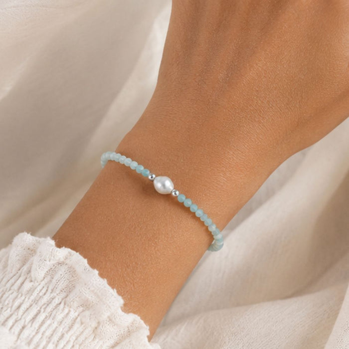 Light blue beaded bracelet with a pearl on a wrist against a neutral background