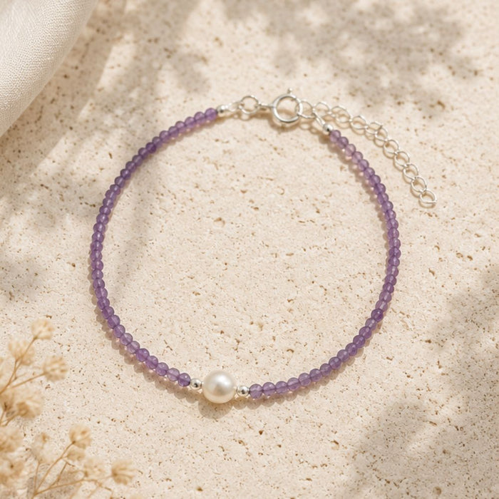 Purple beaded bracelet with a pearl on a beige surface