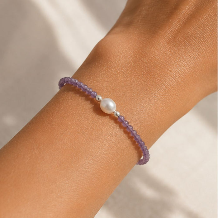 Purple beaded bracelet with a pearl on a wrist against a neutral background
