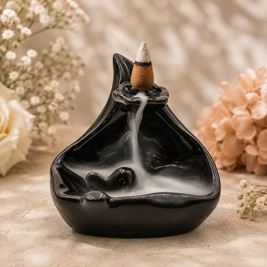 A black ceramic backlit incense burner with a smoking incense cone, set against a warm beige background with soft white and peach flowers.