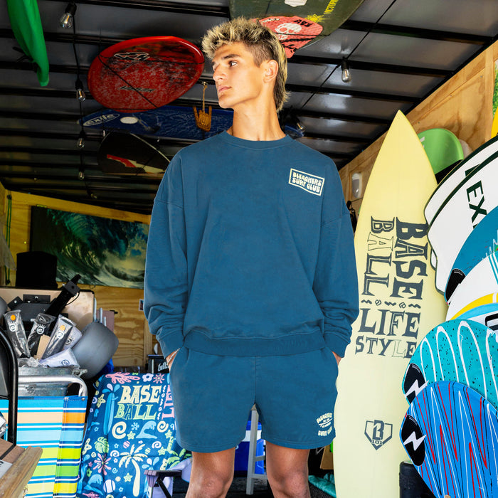 Adult model wearing blue crewneck with "Bleachers Surf Club" design