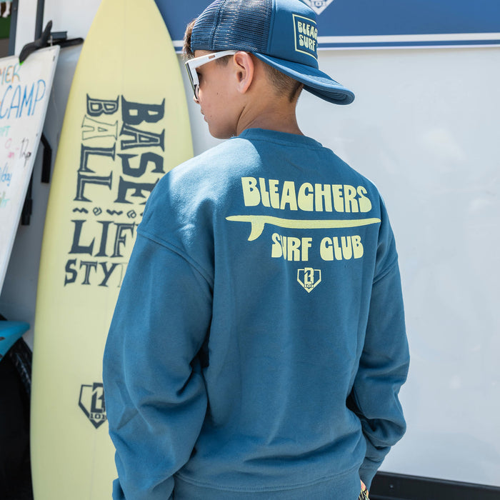 Youth model wearing blue youth crewneck with "Bleachers Surf Club" design