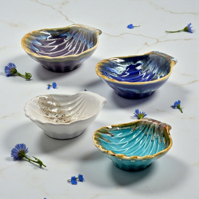 Four ceramic bowls in different colors on a marble surface with small flowers.