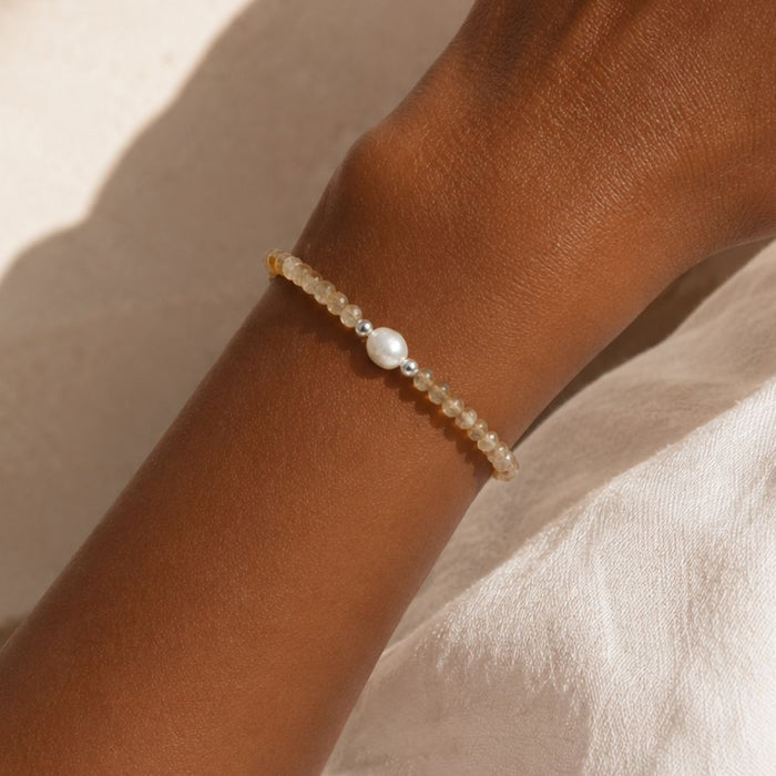 Close-up of a wrist wearing a beaded bracelet with a pearl on a neutral background