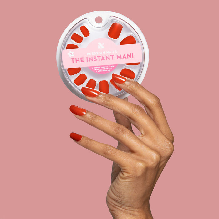 CV - Press-On | Medium | Squoval in vibrant cherry red on hand holding round white packaging on soft pink background