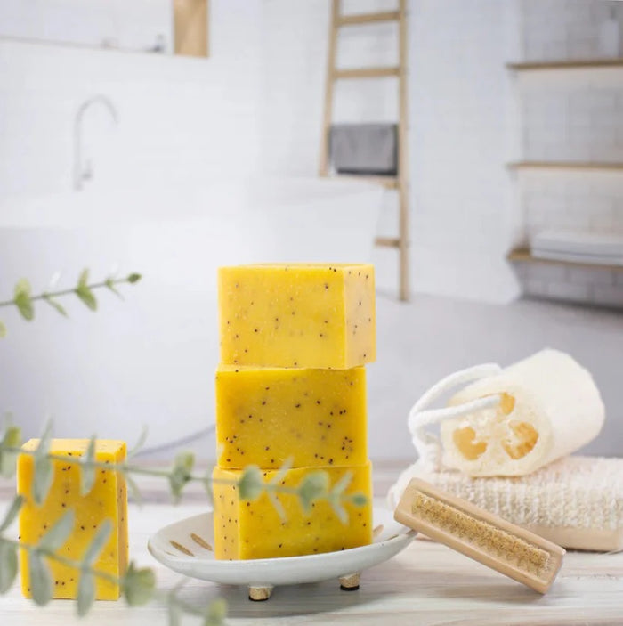 Orange cranberry exfoliating soap bars stacked on a white dish with bath accessories in a bright bathroom