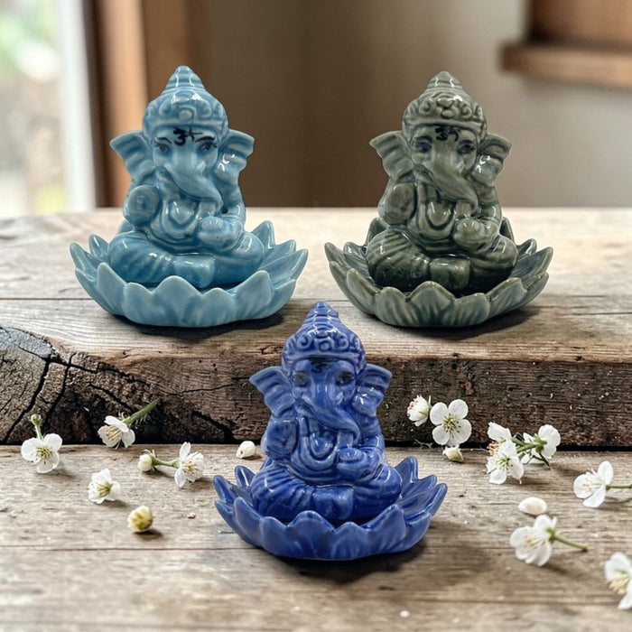 Three colorful Ganesh holders on a wooden surface with flowers.