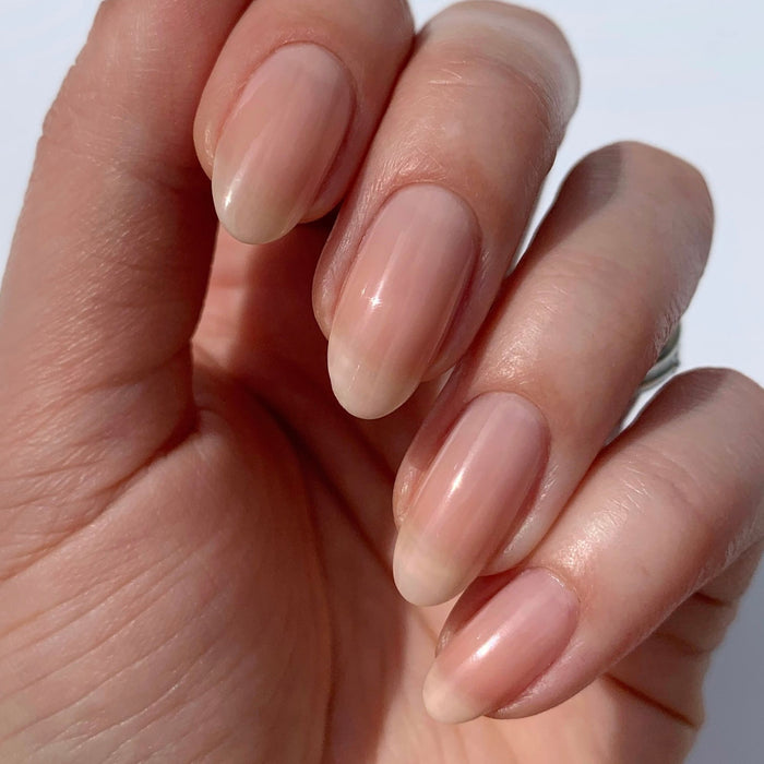 A close-up of a hand with natural, oval-shaped nails, clean and neatly manicured with a subtle finish from LONDONTOWN’s Gel Genius Base Coat, shown against a plain background.