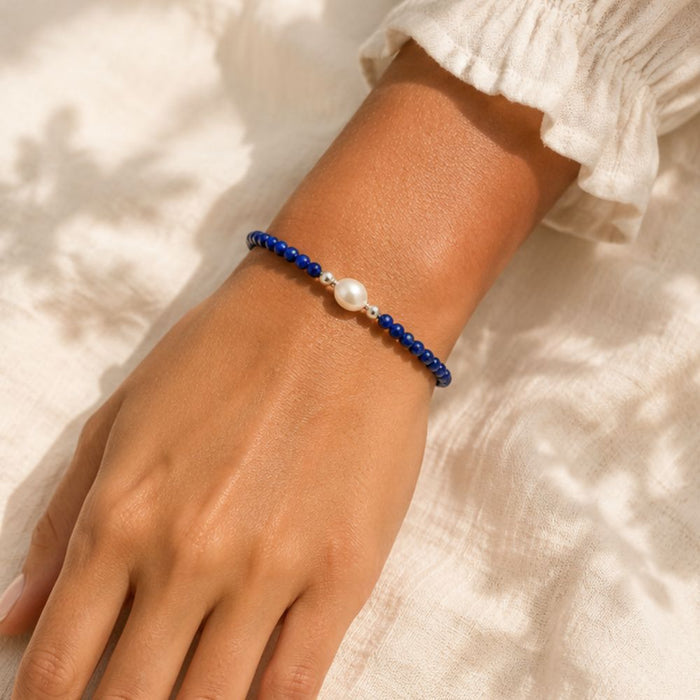 Hand wearing a blue beaded bracelet with a pearl on a light background