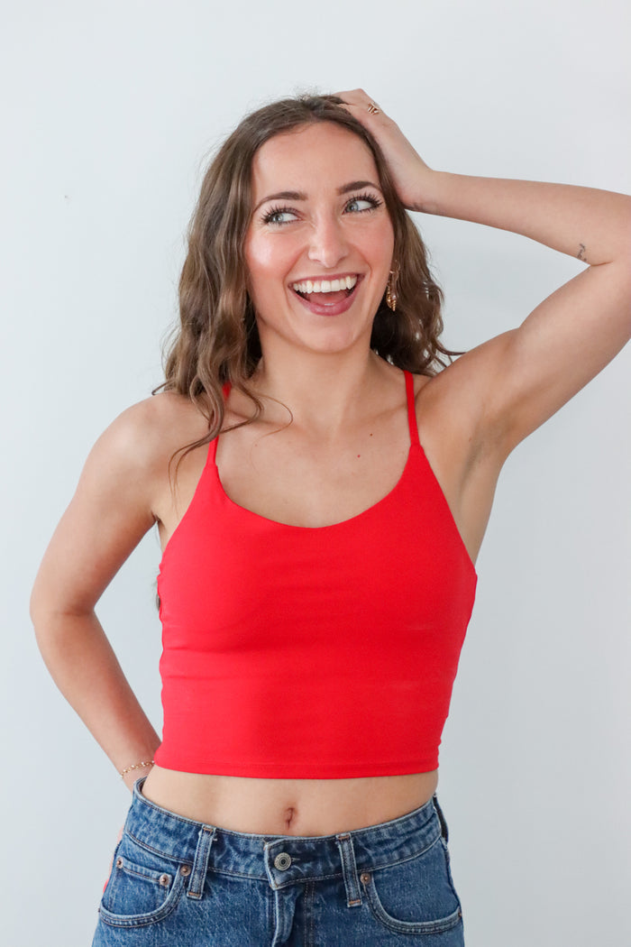 Woman wearing a red tank top and blue jeans against a white background