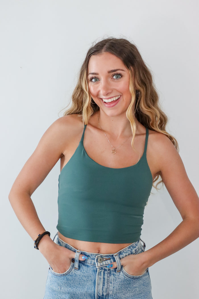 Woman wearing a green tank top and blue jeans against a white background