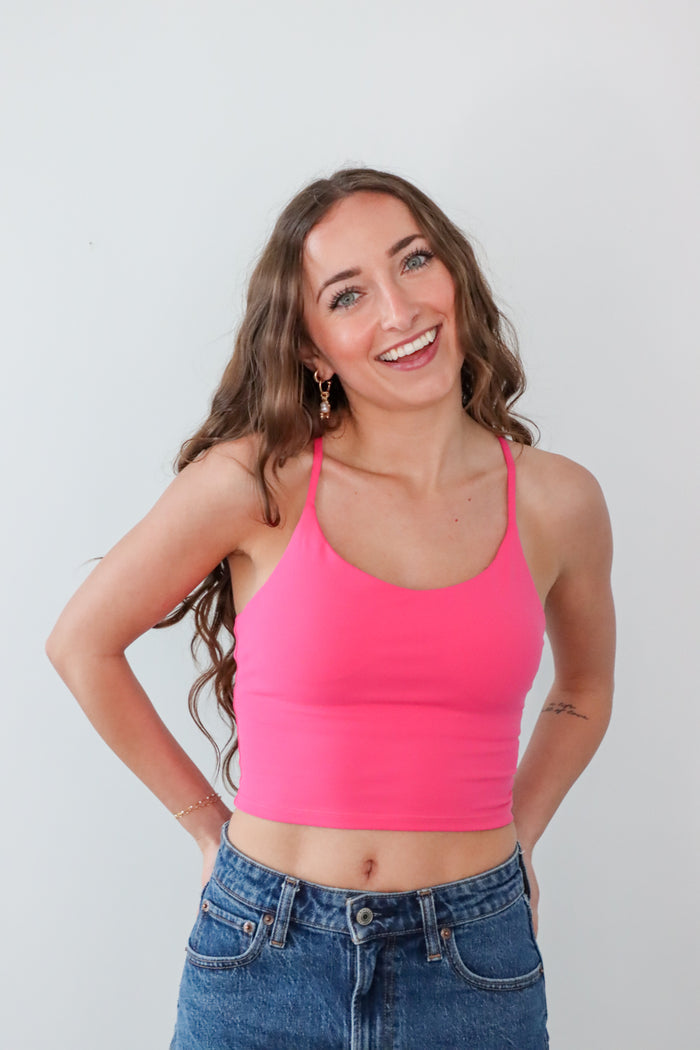 Woman wearing a bright pink crop top and blue jeans against a plain background