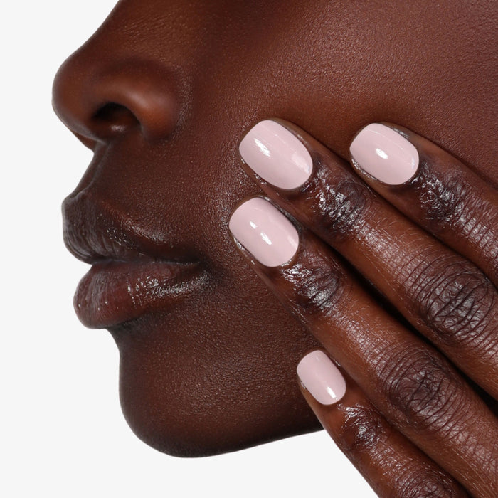 A person touches their face with manicured fingers, showcasing light pink nail polish and LONDONTOWN's Nail Hardener & Base Coat, a 2-in-1 strengthener for flawless beauty.