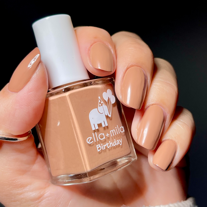Pearl Drops satin top coat over a caramel nude manicure, holding the bottle