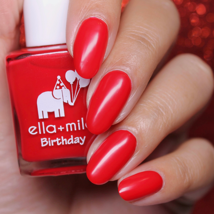 Pearl Drops satin top coat over a bright red manicure, holding the bottle