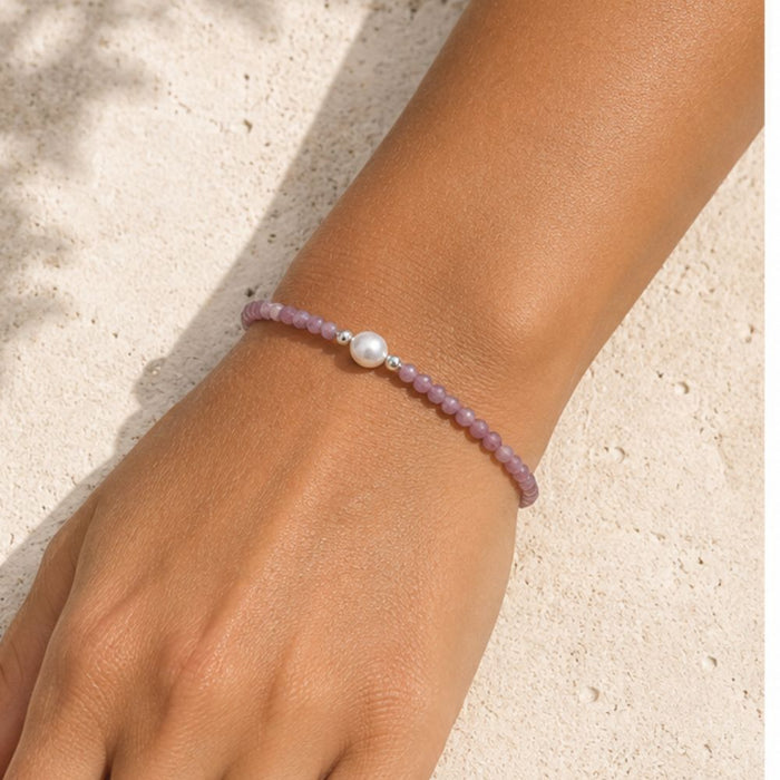Pink beaded bracelet with a pearl on a wrist against a light background