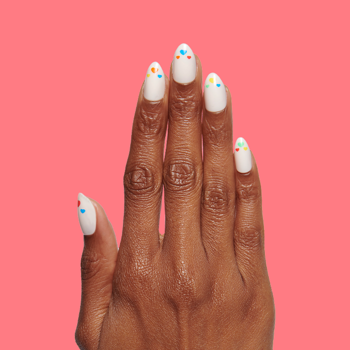 Hand with Rainbow Love | Almond | Medium press-on nails featuring white base and colorful heart details on medium skin tone against coral background
