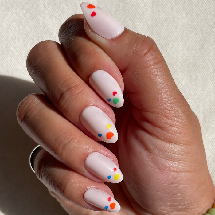 Medium almond press-on nails in soft neutral with small colorful hearts on medium skin tone, Rainbow Love | Almond | Medium