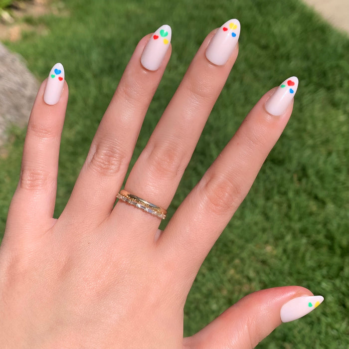 Hand with Rainbow Love | Almond | Medium press-on nails in soft neutral with colorful heart accents outdoors on natural skin tone