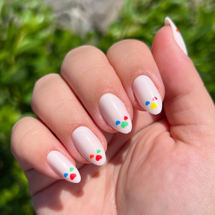Close-up of hand with Rainbow Love | Almond | Medium press-on nails featuring neutral base and scattered colorful heart accents outdoors