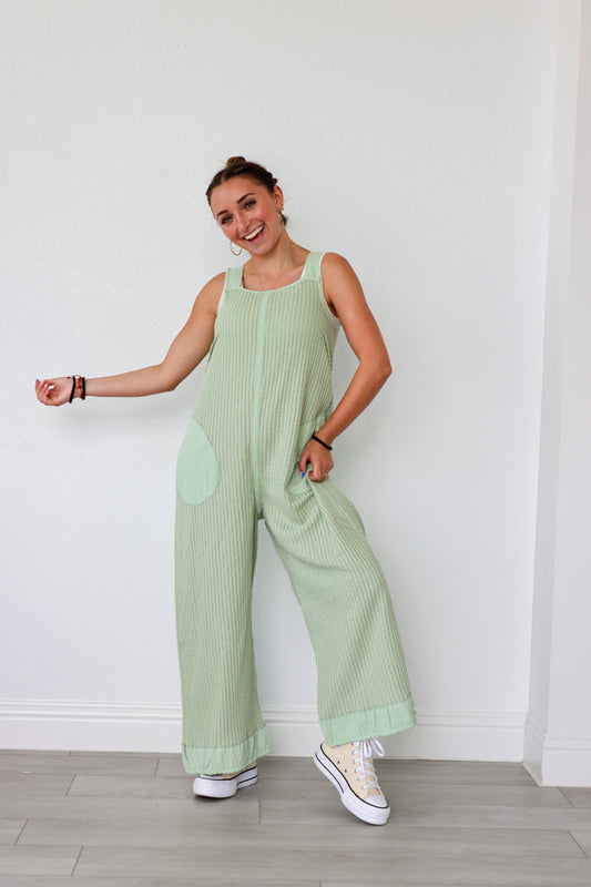 Woman wearing a light green ribbed jumpsuit against a white wall.