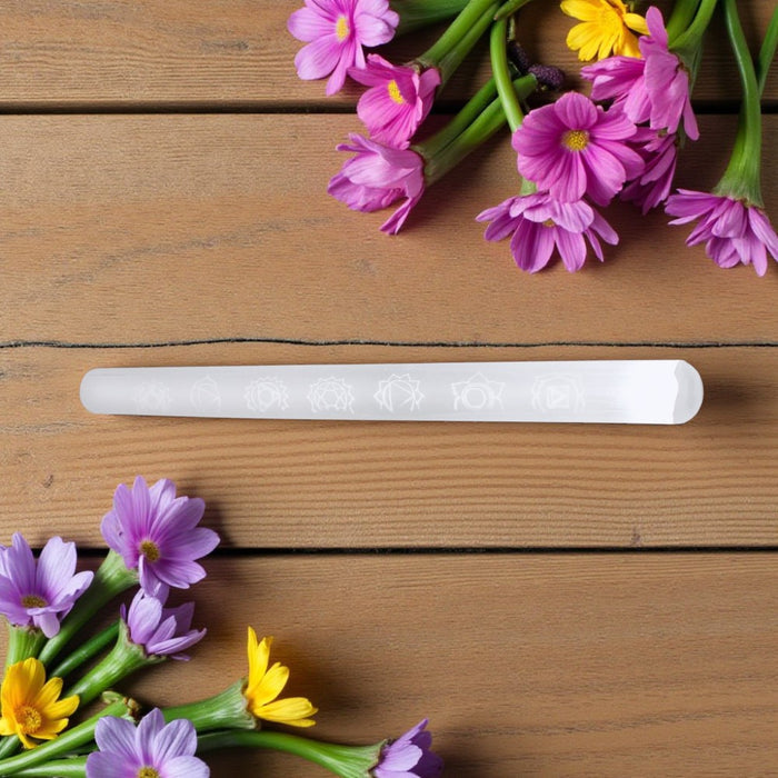 White selenite wand with floral design on a wooden surface with purple and yellow flowers.