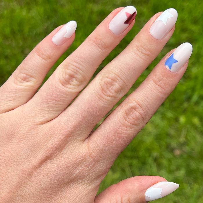 Super Festive Stars | Oval | Medium press-on nails with red, blue, and white star designs on neutral oval false nail manicure