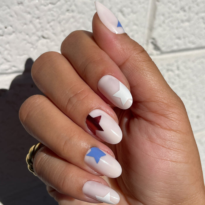 Super Festive Stars | Oval | Medium press-on nails with blue, white, and metallic red star designs on neutral oval tips