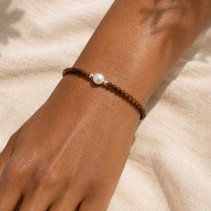 Bracelet with brown beads and a pearl on a wrist against a beige fabric background
