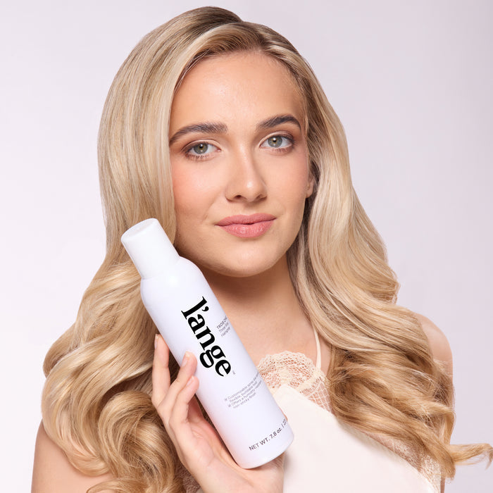 Woman with long, loose waves holding L’ange Trois Chic Three Way Hairspray bottle
