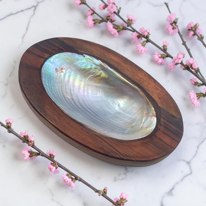 Wooden shell dish with a large shell on a marble surface with pink flowers.